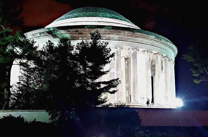 A round, domed memorial glowing white between dark trees