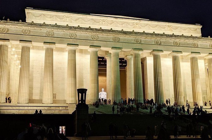 The columned memorial's steps lit up at night, visitors small on the steps